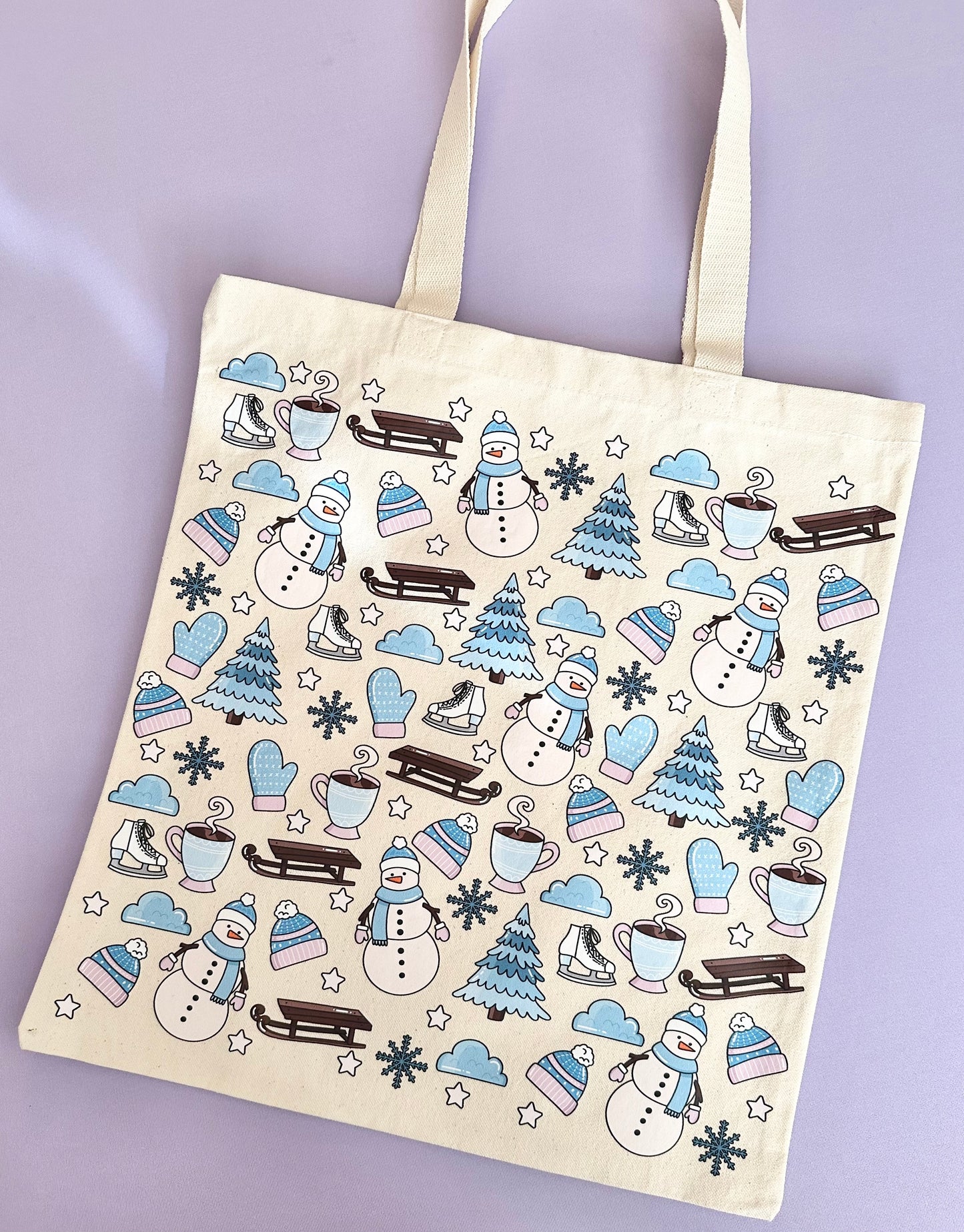 A beige cotton tote bag with a winter snowmen design, featuring illustrations of snowmen, snowflakes, and icy elements.