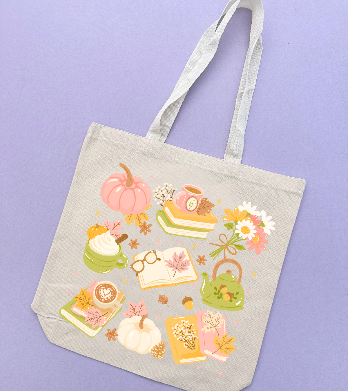 A light beige canvas tote bag with long handles, decorated with a colorful autumn-themed illustration featuring pumpkins, books, flowers, and a teapot, displayed against a solid lavender background.