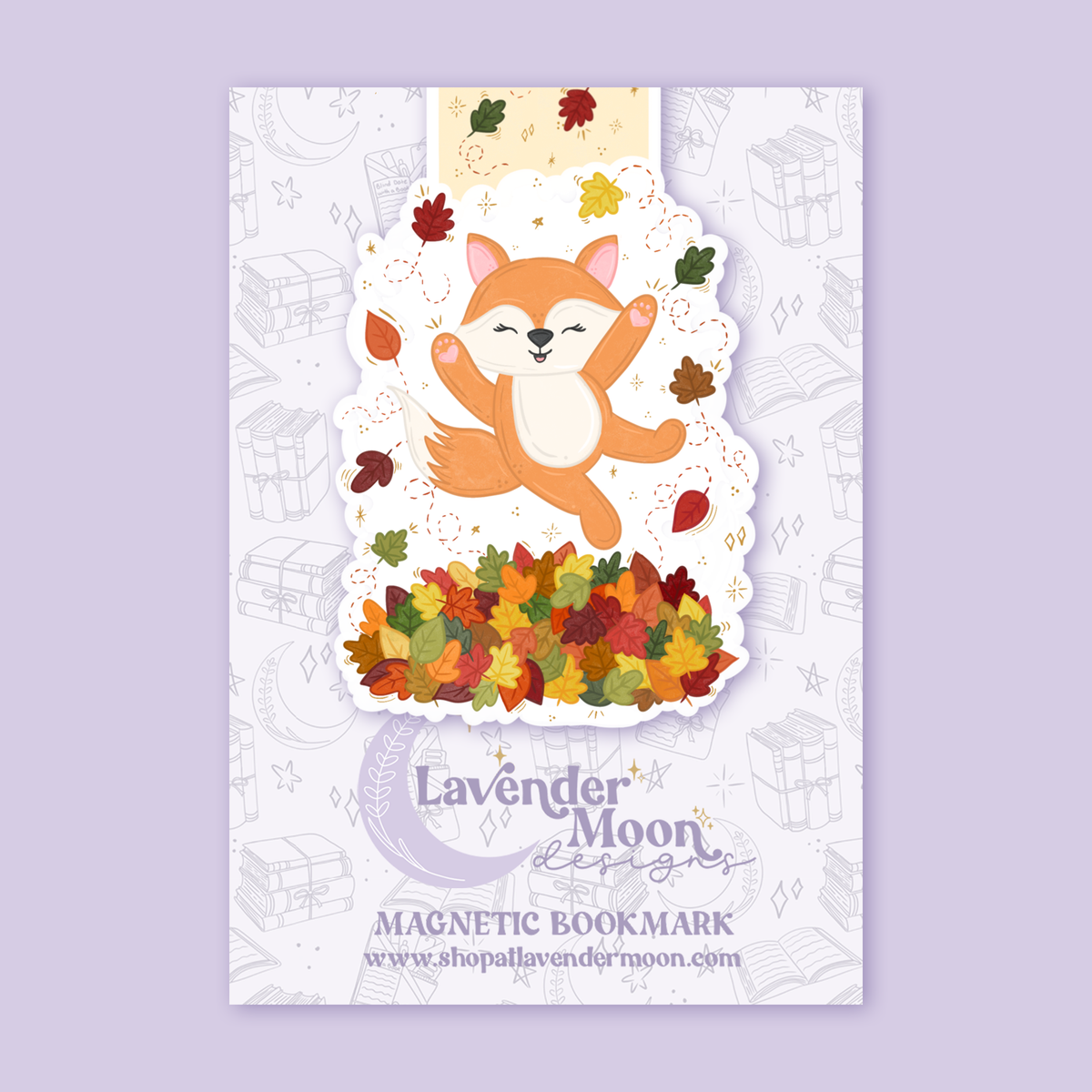 Product photo of a magnetic bookmark on a light purple background. The magnetic bookmark is a illustration of a fox jumping in a pile of fall leaves.