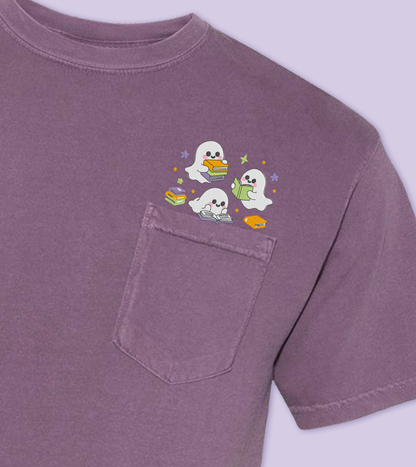 A dark purple short-sleeve pocket t-shirt featuring a small embroidered cartoon graphic of a three ghosts reading  peeking out of the chest pocket, set against a matching light purple background.